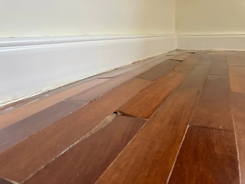 Close view of buckled hardwood flooring at a wall